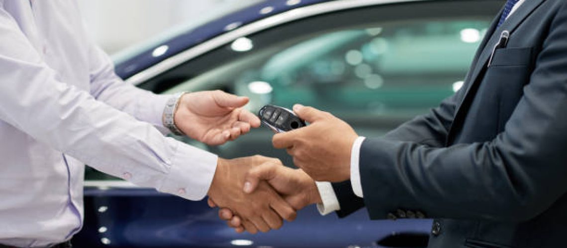 Salesman giving car keys to customer and shaking his hand